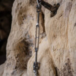 Climbing anchor fixed to a rock wall with a hanging steel carabiner and hardware.