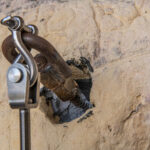 Rusty anchor bolt and clamp embedded in a drilled hole in a concrete wall.