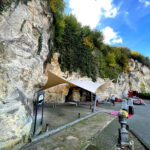 Rock cliff with ivy overhead; a light tan and white canopy shelters a small outdoor work/setup area near a cave opening in the rock.