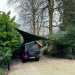 Black SUV parked in a gravel driveway under a triangular black shade sail attached to two posts.