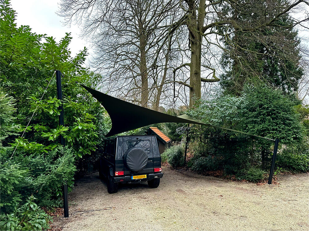 Black SUV parked in a gravel driveway under a triangular black shade sail attached to two posts.