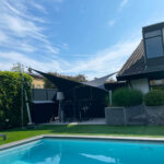 Backyard with a rectangular blue pool, dark privacy fencing, and a seating area under black triangular shade sails.