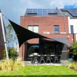 Modern brick house with solar panels on the sloped roof; outdoor dining table and chairs beneath black shade sails in the yard.