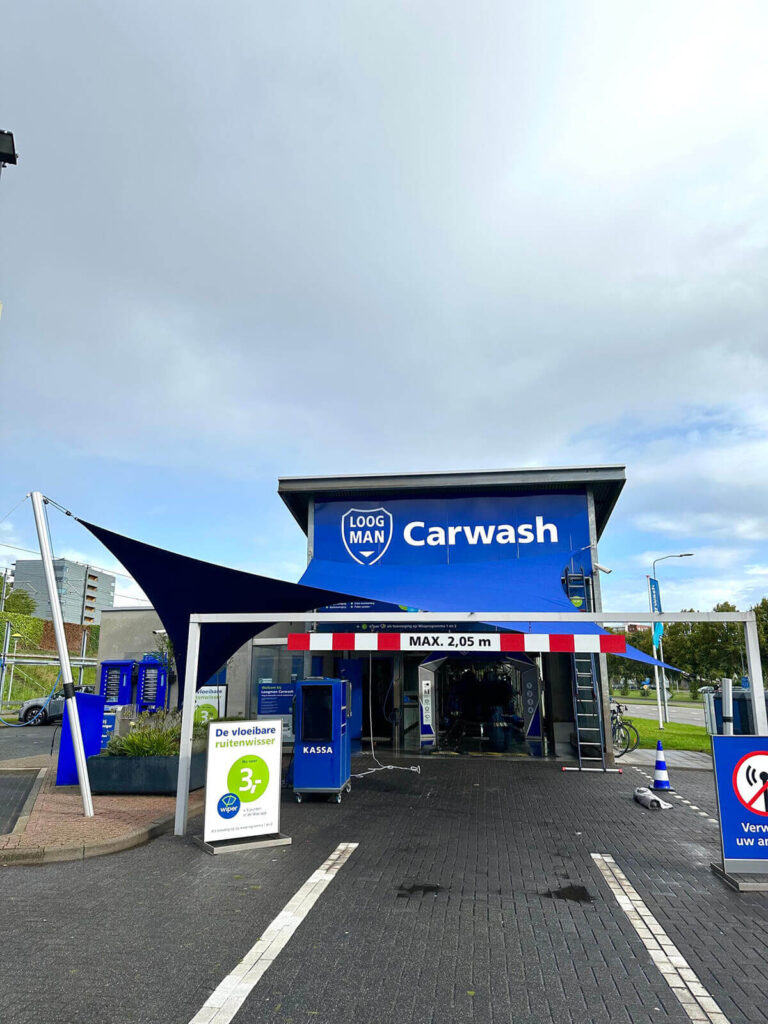 Blue car wash entrance with a large sign reading ‘Carwash’ and a height limit bar reading ‘MAX. 2,05 m’ in red and white.