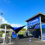 Car wash facility with a large blue canopy and blue signage reading 'Carwash' at an outdoor station under a clear blue sky