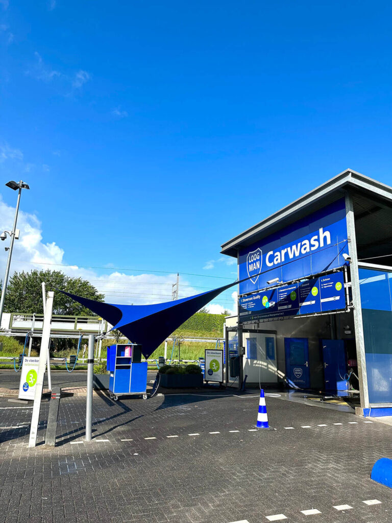 Car wash facility with a large blue canopy and blue signage reading 'Carwash' at an outdoor station under a clear blue sky