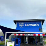 Blue carwash building with a curved dark canopy and a large 'Carwash' sign on a blue facade.