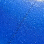 Close-up of blue fabric with a diagonal zigzag seam and water droplets on its surface.