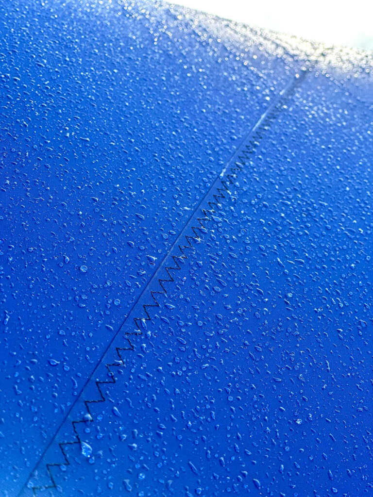 Close-up of blue fabric with a diagonal zigzag seam and water droplets on its surface.