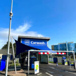 Carwash entrance with a blue canopy and a sign that reads 'Carwash' and a height limit bar marked 'MAX. 2,05 m' in front of a modern building.