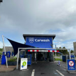 Carwash entrance with a blue awning and LOOG MAN Carwash sign above, visible payment kiosk and signs at the front.