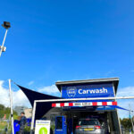 Carwash entrance with blue sign reading 'Carwash' and a gray SUV parked inside, height barrier showing 'MAX. 2,05 m' above the doorway