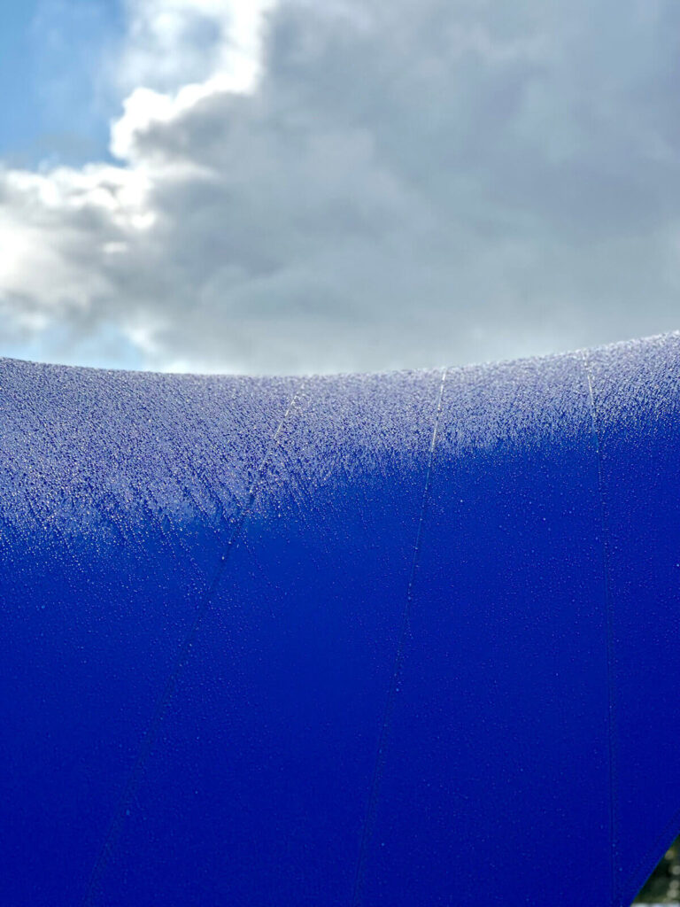 Close-up of a vivid blue curved surface with frost-like droplets, cloudy sky in the background.