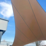 Curved brown fabric canopy above a glass entrance against a blue sky.