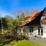 White house with orange tiled roof and a large black tensile shade sail over a patio with white chairs outside