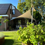 Brick house with solar panels on the roof, patio dining area, and a hanging plant basket in the foreground.