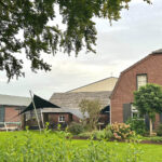 Brick house with a gabled roof, shaded seating under a triangular sail, and a manicured garden in the yard.