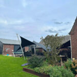 Backyard scene with three dark triangular shade sails over a seating area near brick houses and a green lawn.