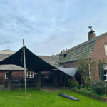 Backyard with black fabric shade sail over a brick patio near a house and green lawn.