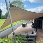 Backyard patio shaded by a large beige sail shade attached to metal poles, over outdoor seating.