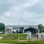 Modern community building with solar panels, shaded outdoor area, and a Start banner by the entrance stairs.