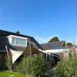 Suburban house with solar panels on a sloped roof, white shade sails over a patio, and a clear blue sky above.