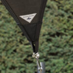 Close-up of a black fabric strap with a white triangular Manta Roofs logo patch, outdoors in greenery.