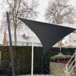 Black triangular shade sail mounted between posts over a snowy backyard.