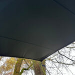 Underside of a dark outdoor canopy or tent roof with tree trunks and branches visible below.