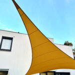 Large yellow fabric shade sail arching from a building against a bright blue sky.